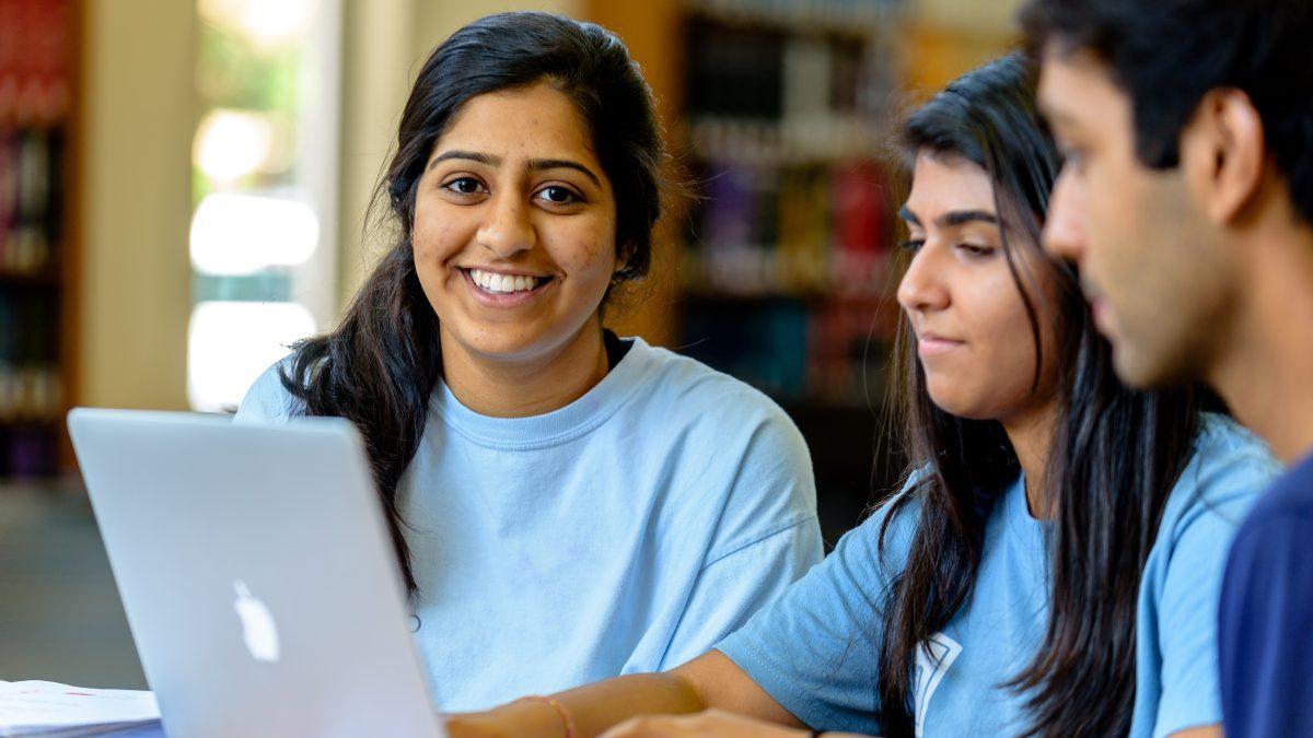 A male student and two female students work on a computer in a U.N.C. library.