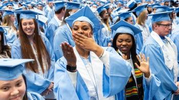 Graduate in cap and gown blows kisses to the crowd in midst group of graduates