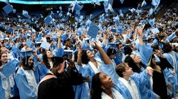 Graduates of U.N.C Chapel Hill in regalia throwing up their caps in Winter Commencement in the Dean E. Smith Center.