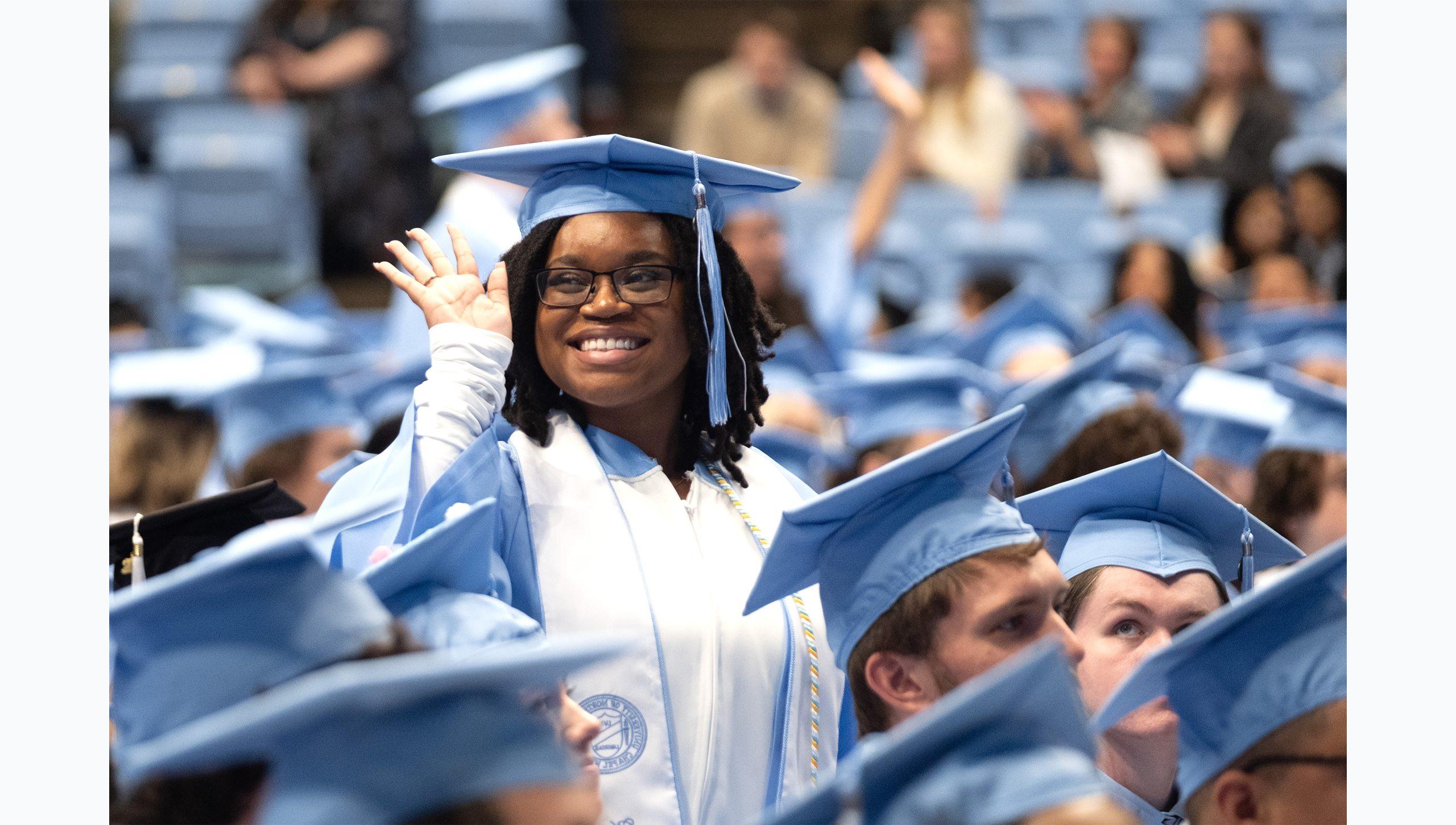 A female student smiling and waving from the crowd at U.N.C. Chapel Hill's Winter Commencement.